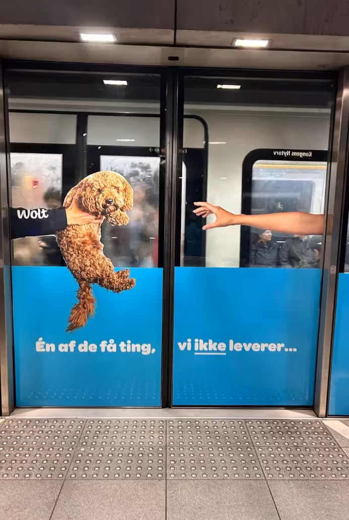En Wolt reklame på en metrostation. Det er en hund, der rækkes ud